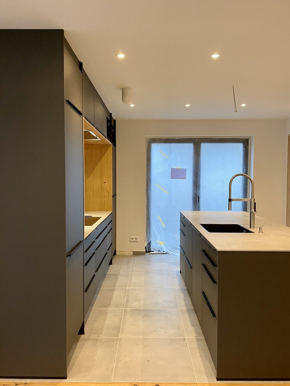 Modern kitchen: island with sink, dark cabinets, construction foil on door, unfinished.
