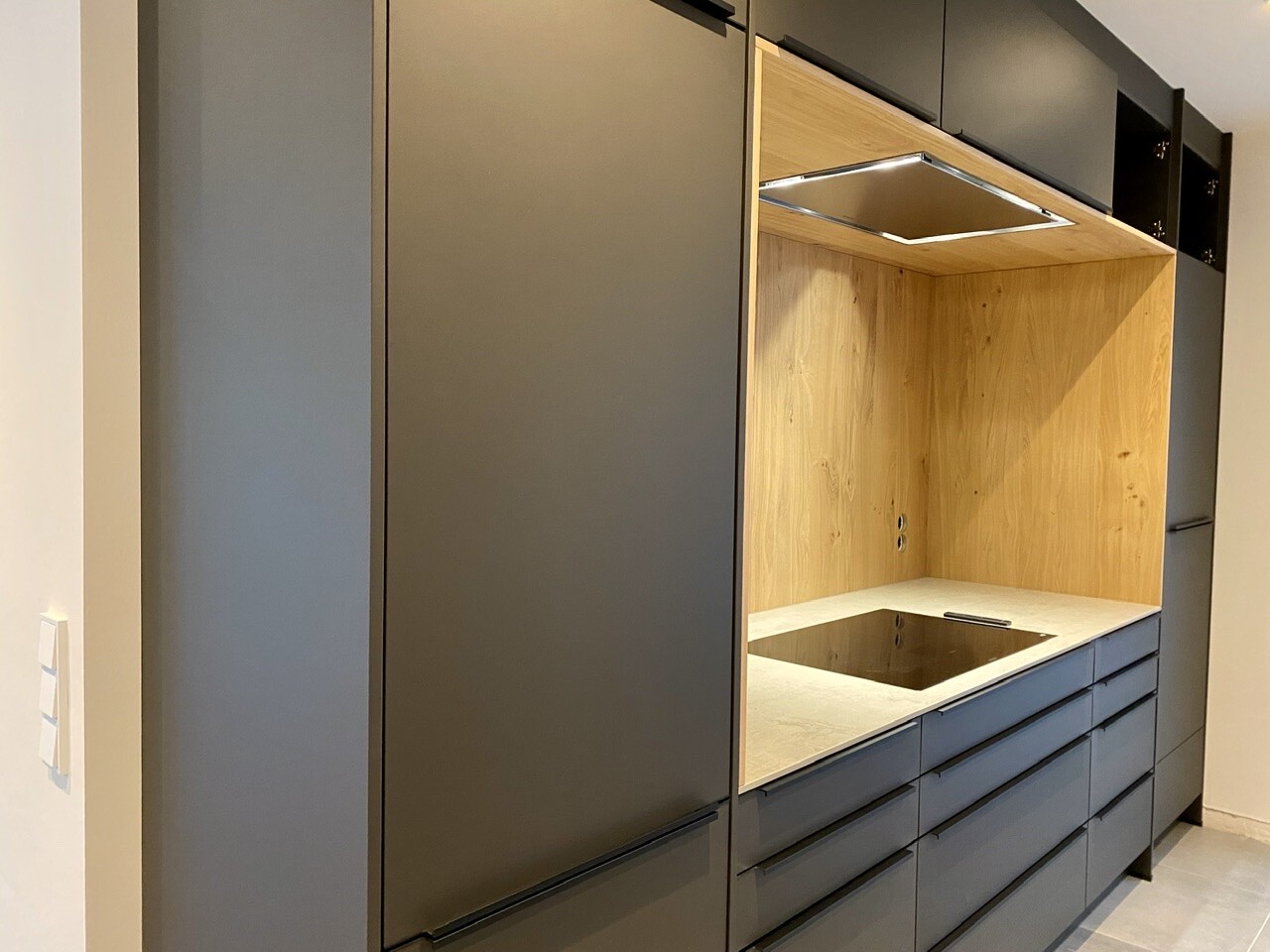 Modern kitchen cabinets in dark gray, open wooden niche with induction cooktop and extractor hood
