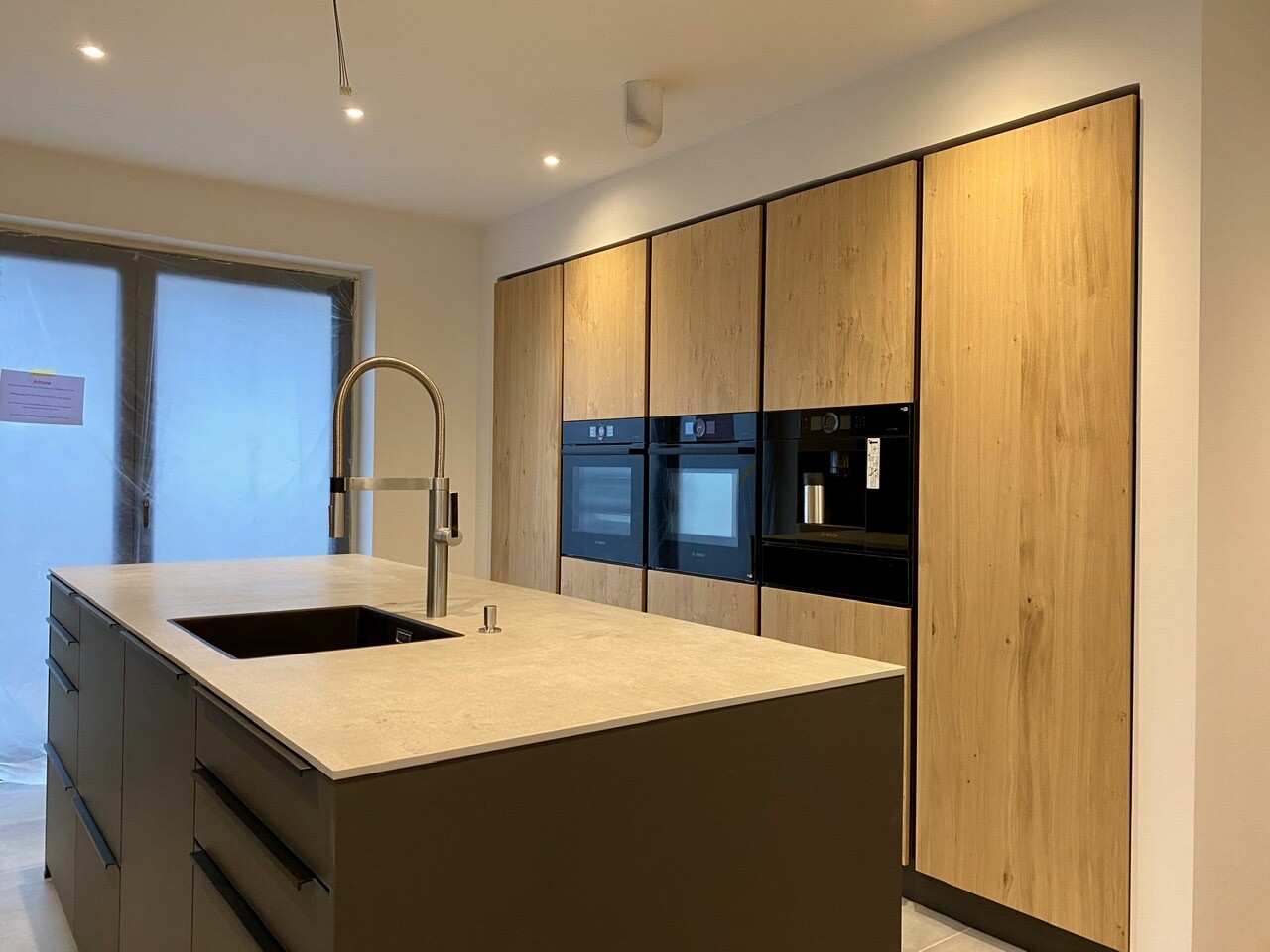 Modern kitchen with island, sink and faucet, wooden fronts, integrated ovens.