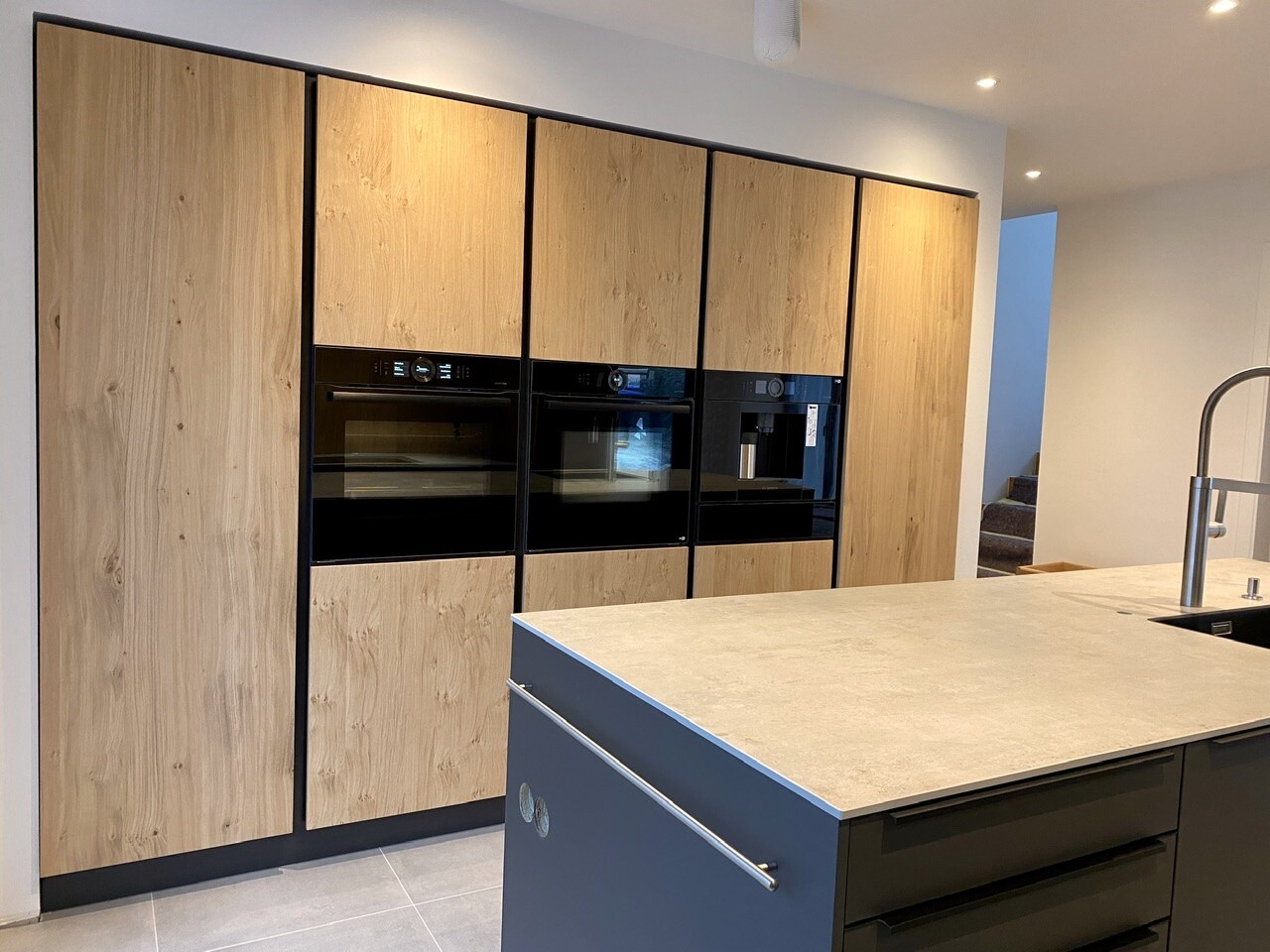 Modern kitchen with wooden fronts, integrated ovens and cooking island with sink.