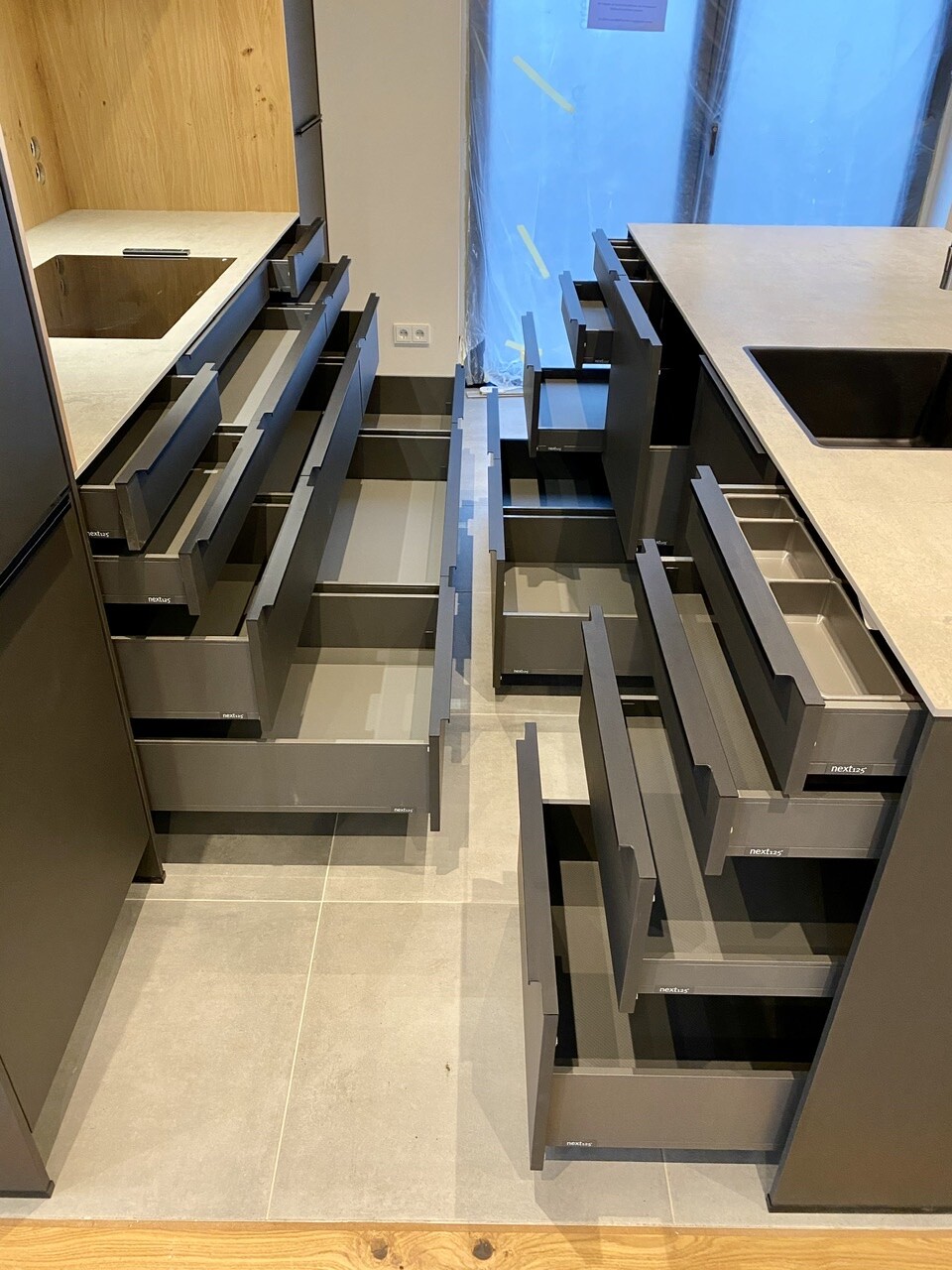 Modern kitchen with many open gray drawers; sink on the right, window with protective foil.