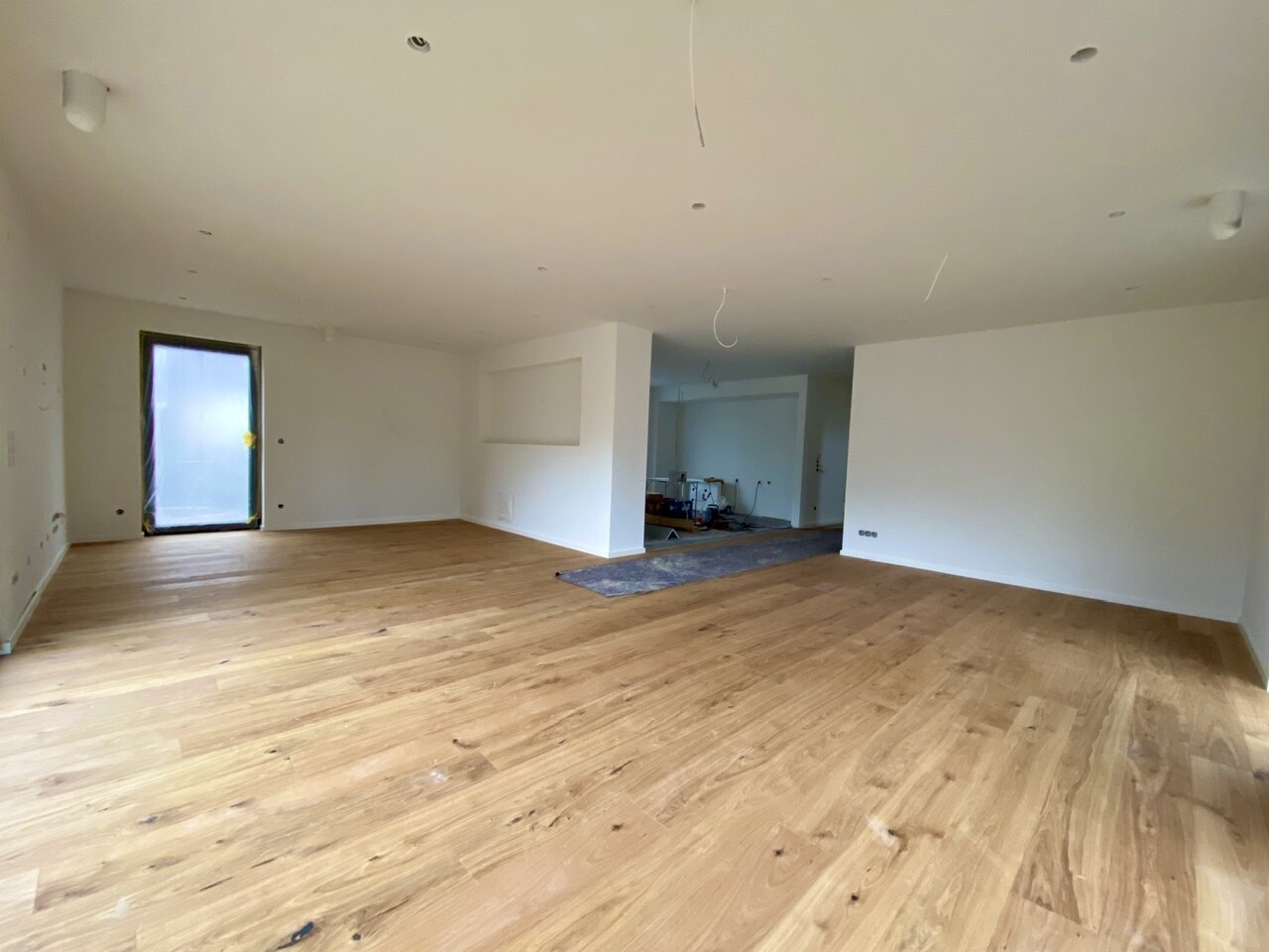 Bright living space with wooden floor, open doorway, and construction work in the background.