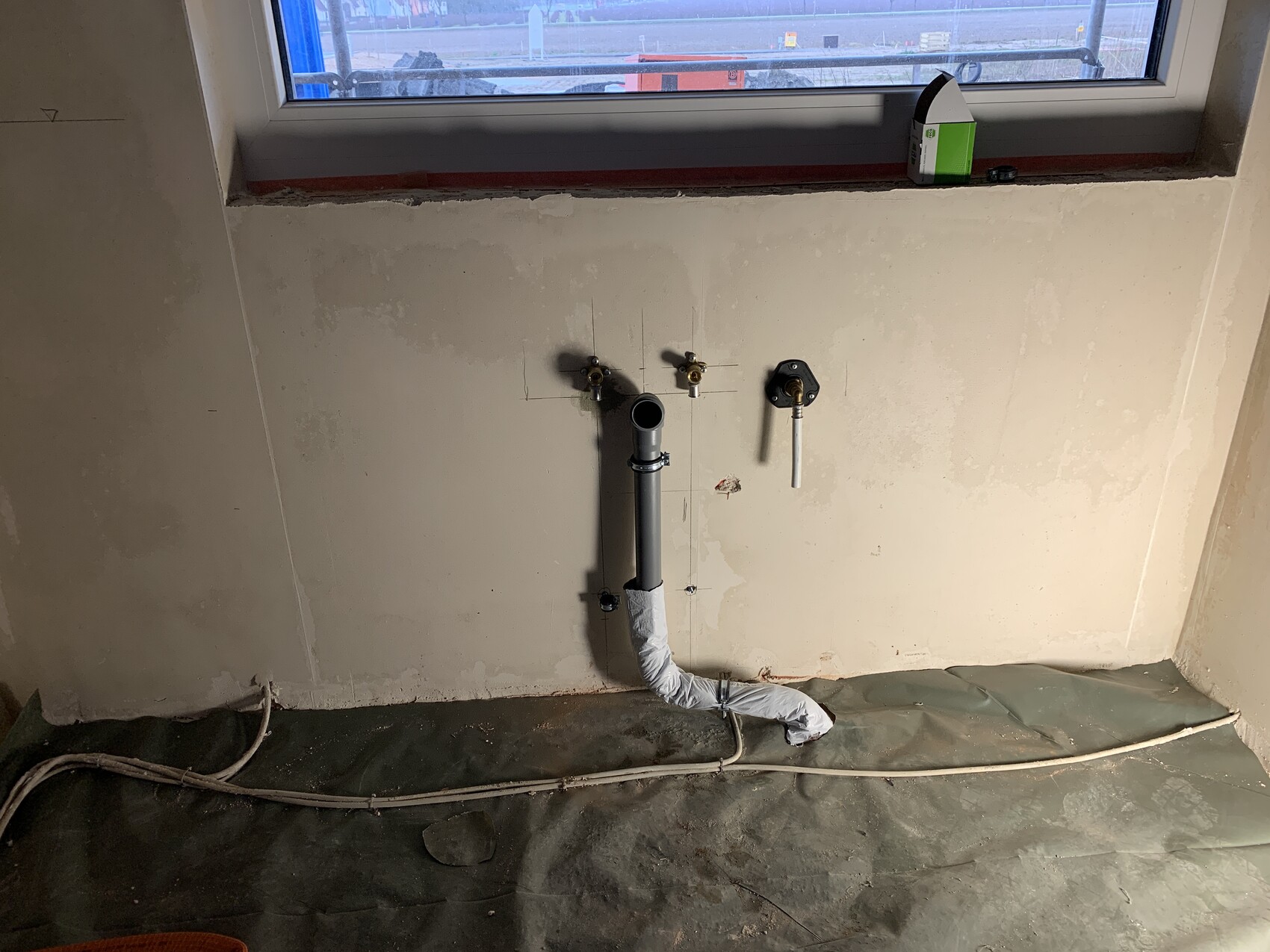 Exposed plumbing installation on wall: drain pipe, two valves, insulated pipe, and window above.