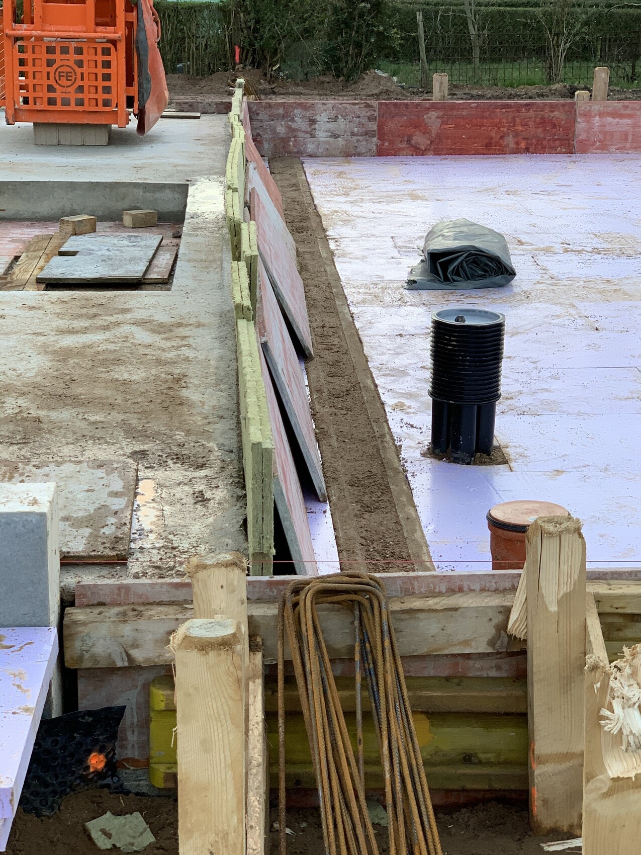 Construction site: foundation formwork with wooden frame, insulation boards, and black pipe.
