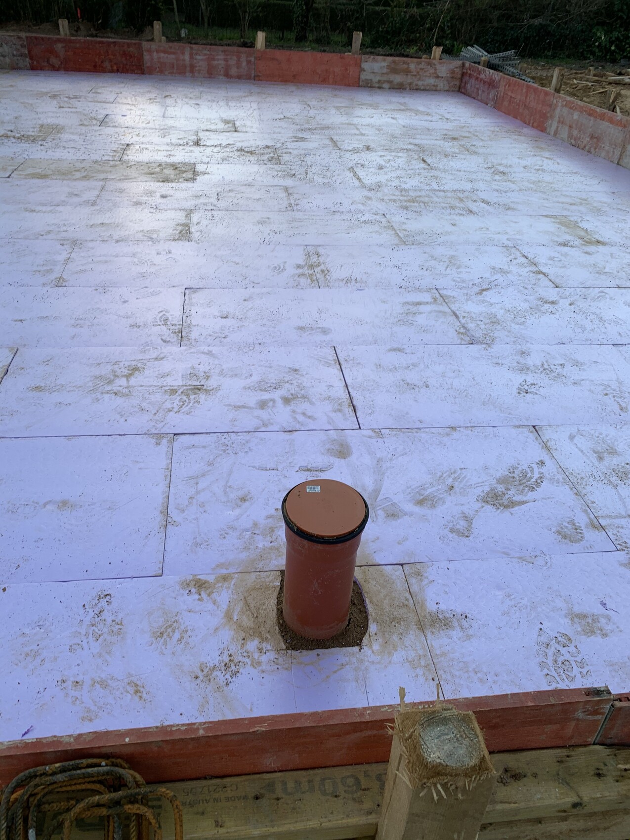 White insulation boards on building base, red pipe stub in the middle, footprints on the ground.