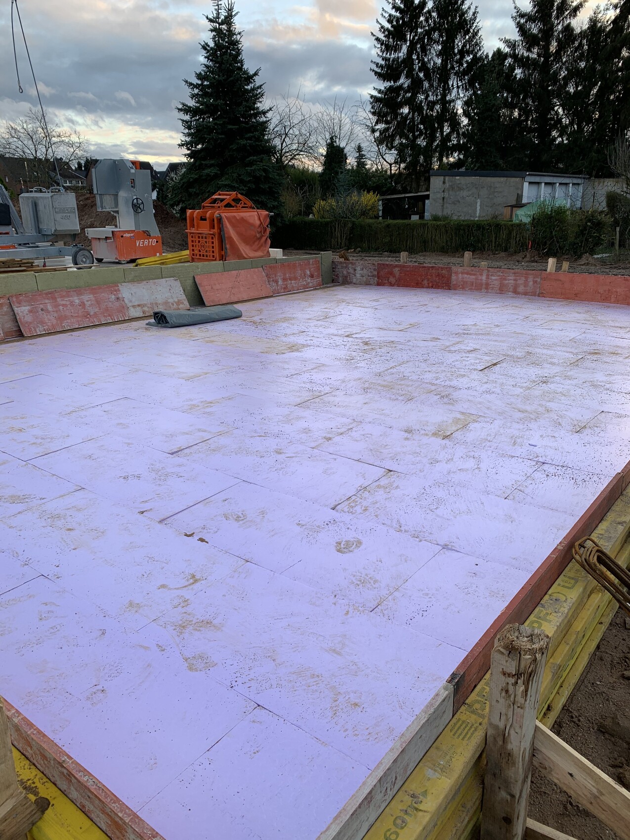 Excavation pit with foundation slab and purple insulation boards, framed by wooden boards.