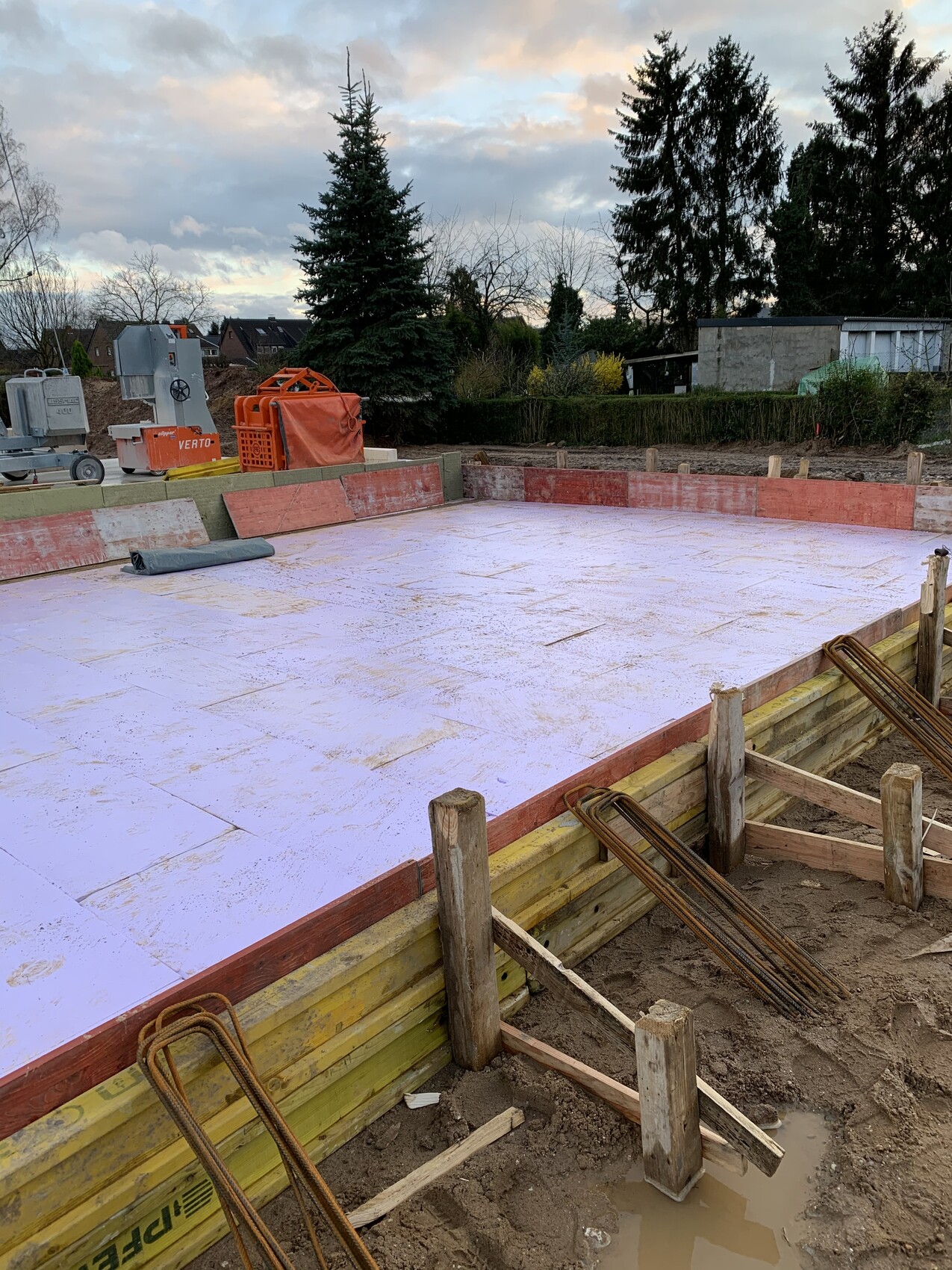 Construction site with foundation made of purple insulation boards, wooden formwork and steel reinforcement.