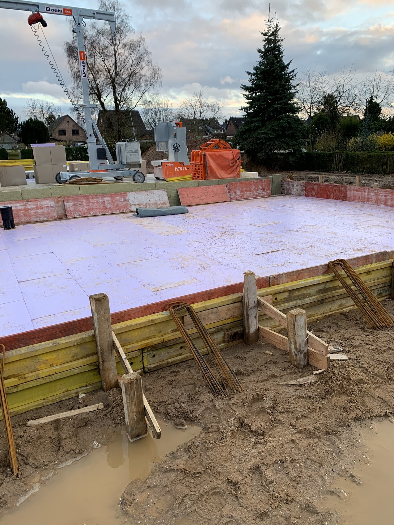Foundation slab being prepared: formwork, reinforcing steel, construction crane and machinery.