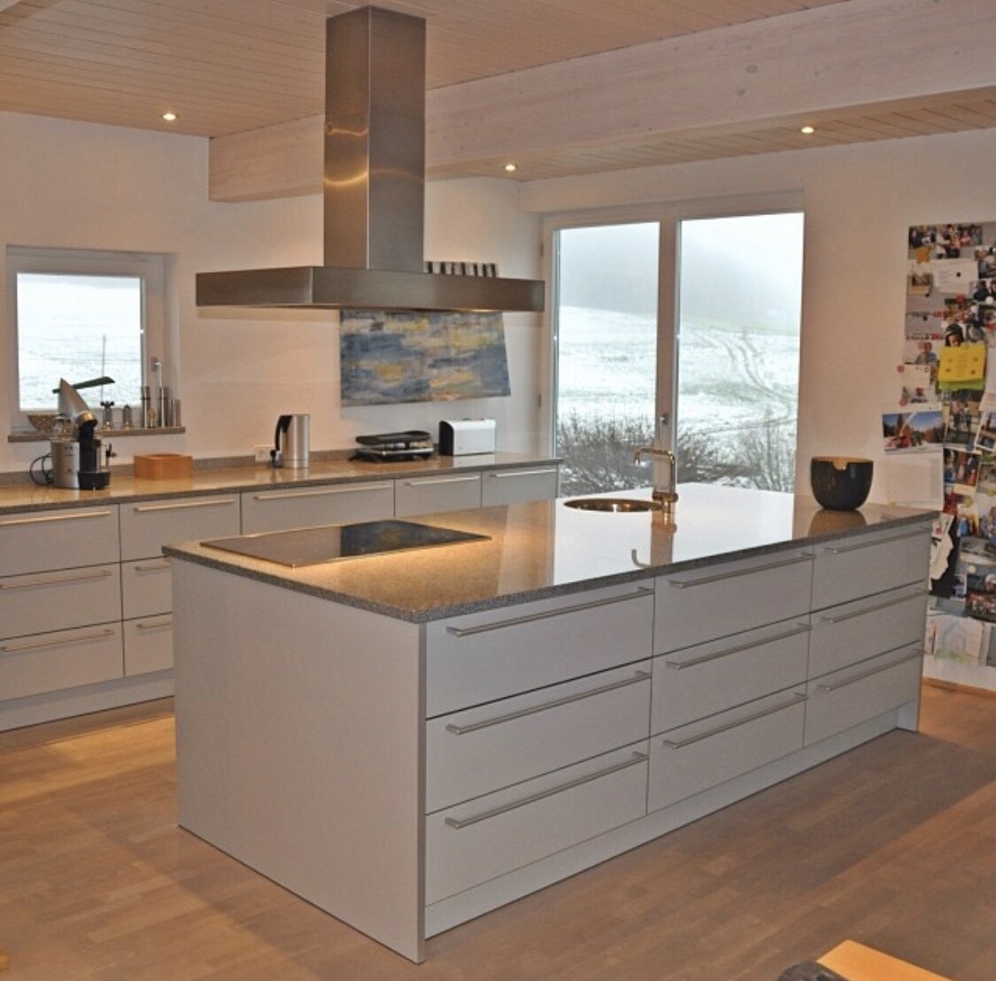Modern kitchen with island, extractor hood, white cabinets, view of snow-covered landscape.