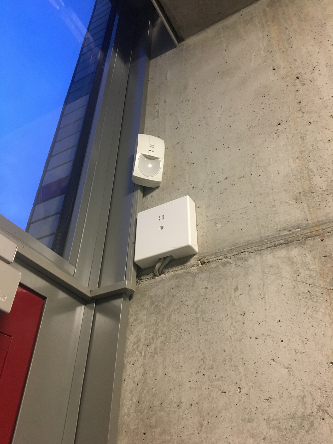 Wall-mounted safety sensors and alarm box on a raw concrete wall next to a window