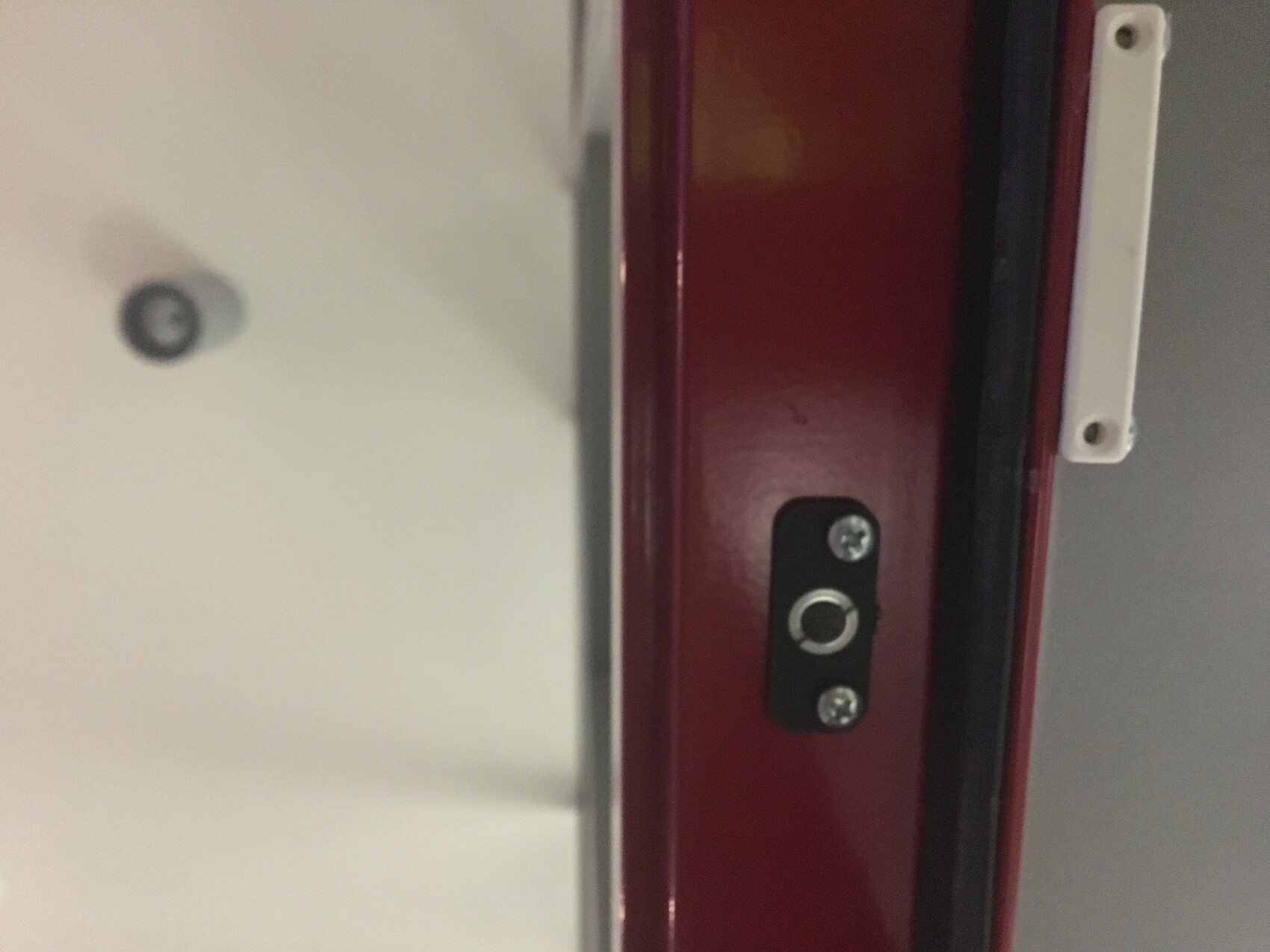 Close-up of a red door frame with a black metal locking plate and screws
