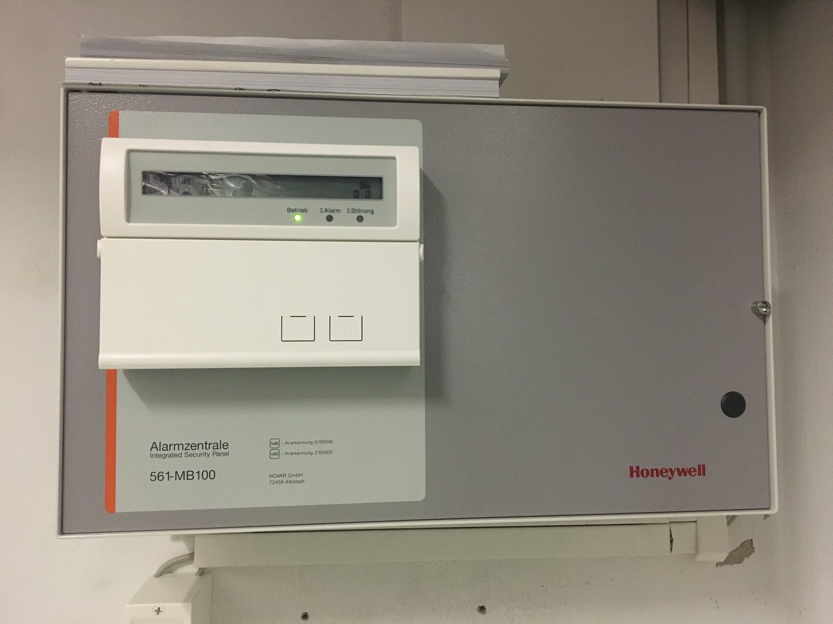 Honeywell alarm control panel with display, two buttons, and green status light, mounted on the wall.