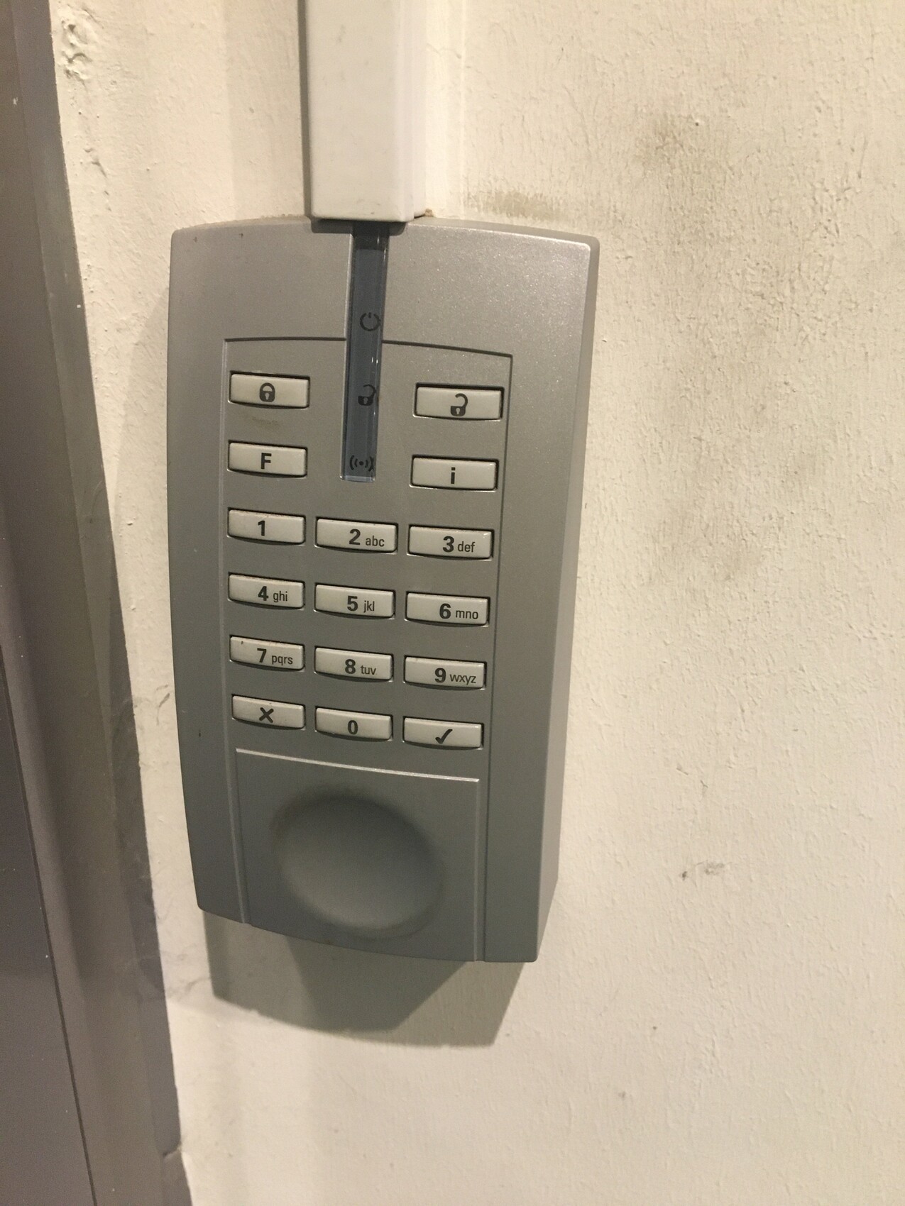 Gray door access keypad with numeric pad on white wall.