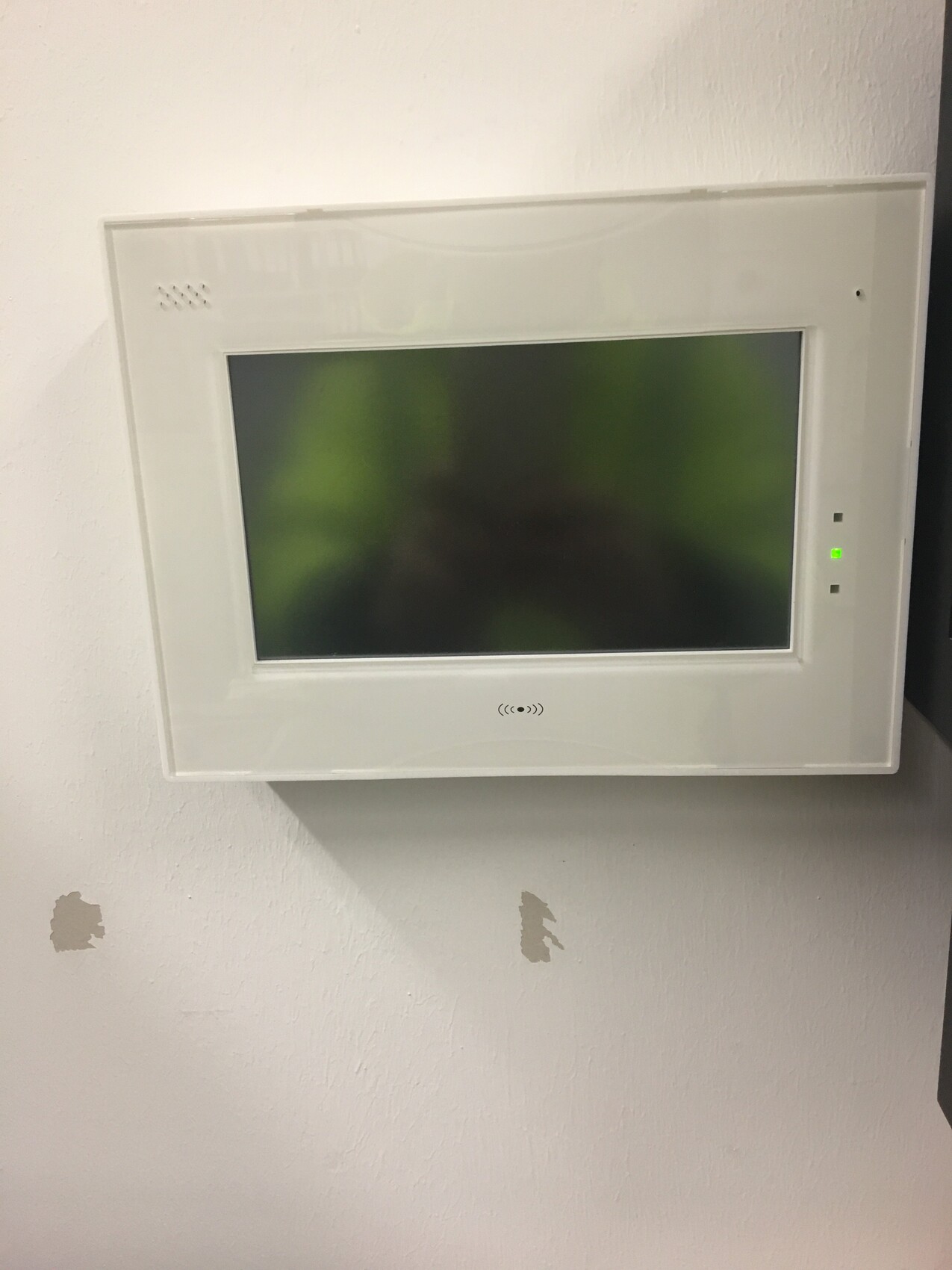 White wall monitor with large display, mounted on the wall; green LED on the right.
