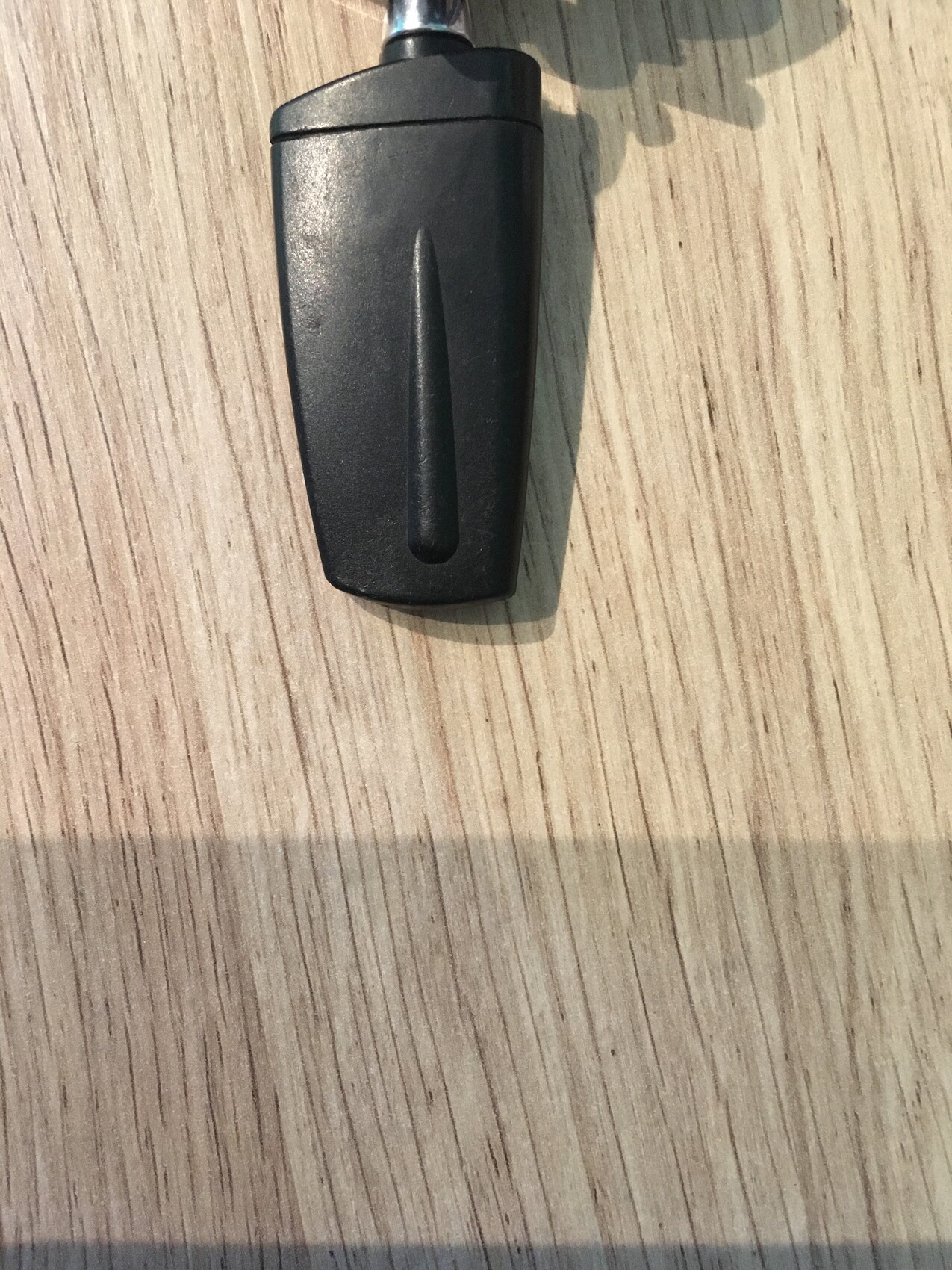 Black plastic part with metal rod on wooden surface