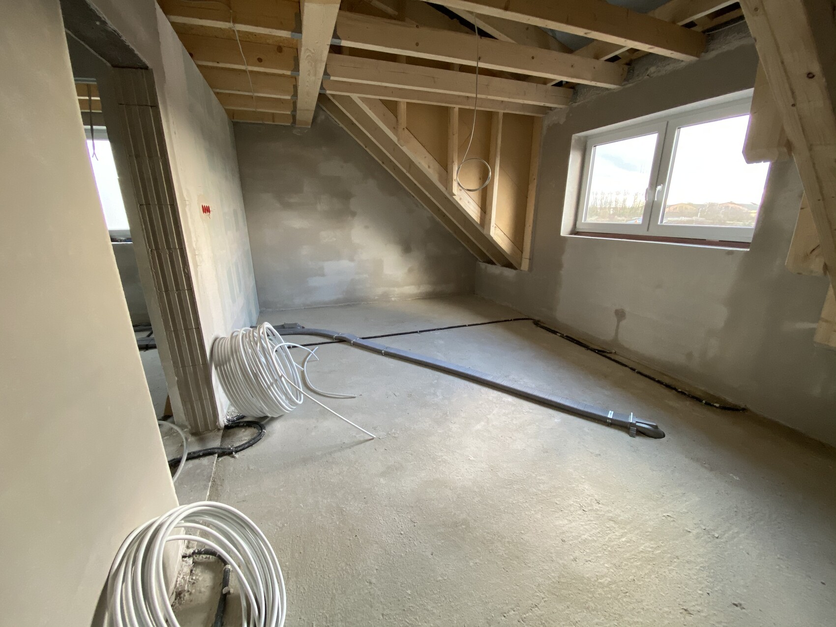 Renovierungsraum im Dachgeschoss mit sichtbarem Dachstuhl, Kabelrollen und Fenster