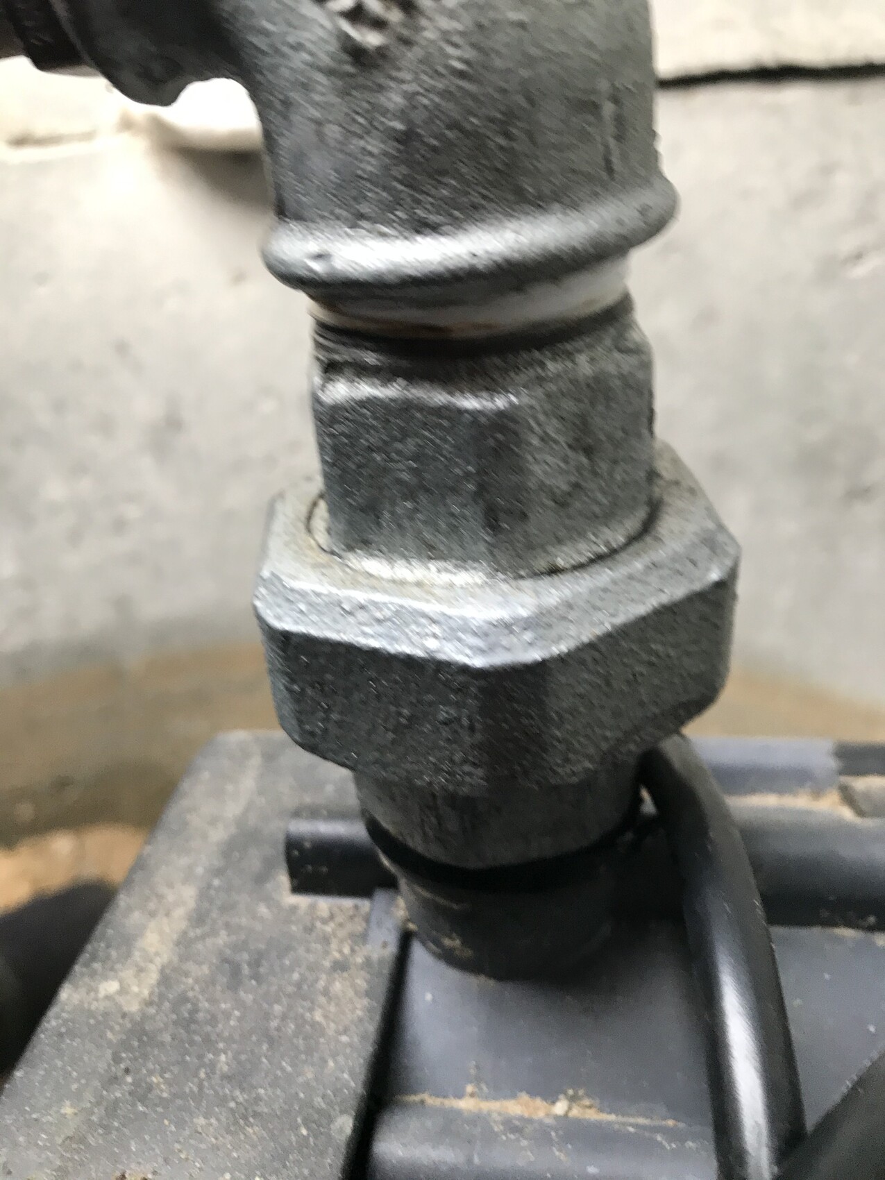 Close-up of a dirty metal pipe connection with hex nut and gasket.