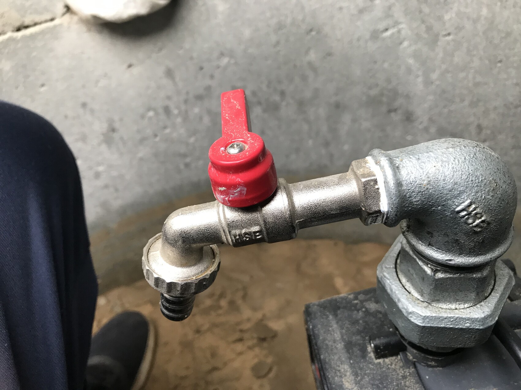 Metal pipe with red valve handle and screw fitting in front of concrete floor.