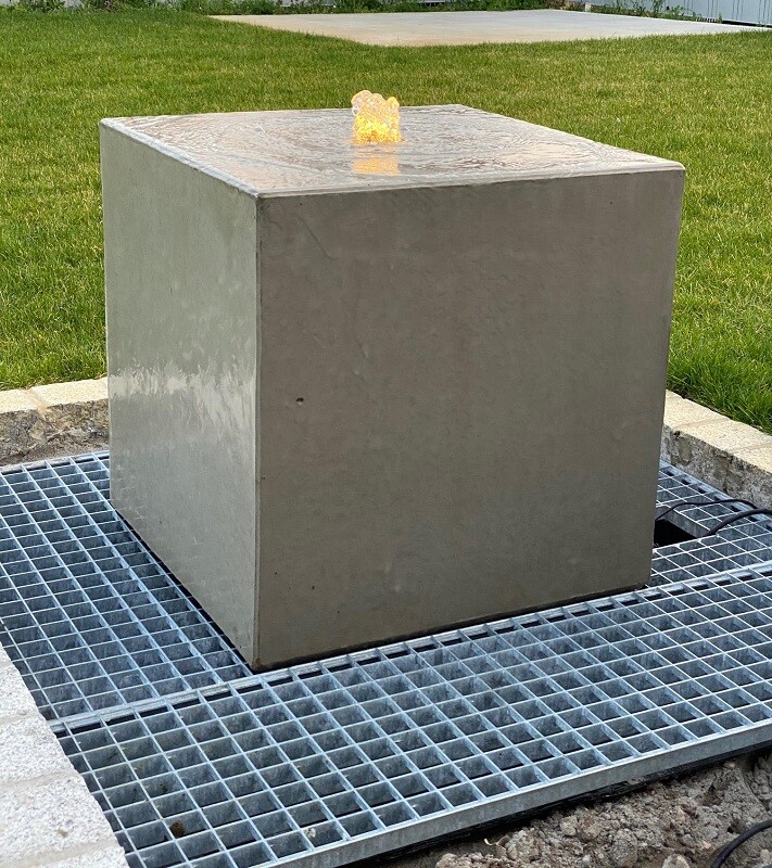 Gray cube-shaped metal block on metal grid, water collecting on the top surface.