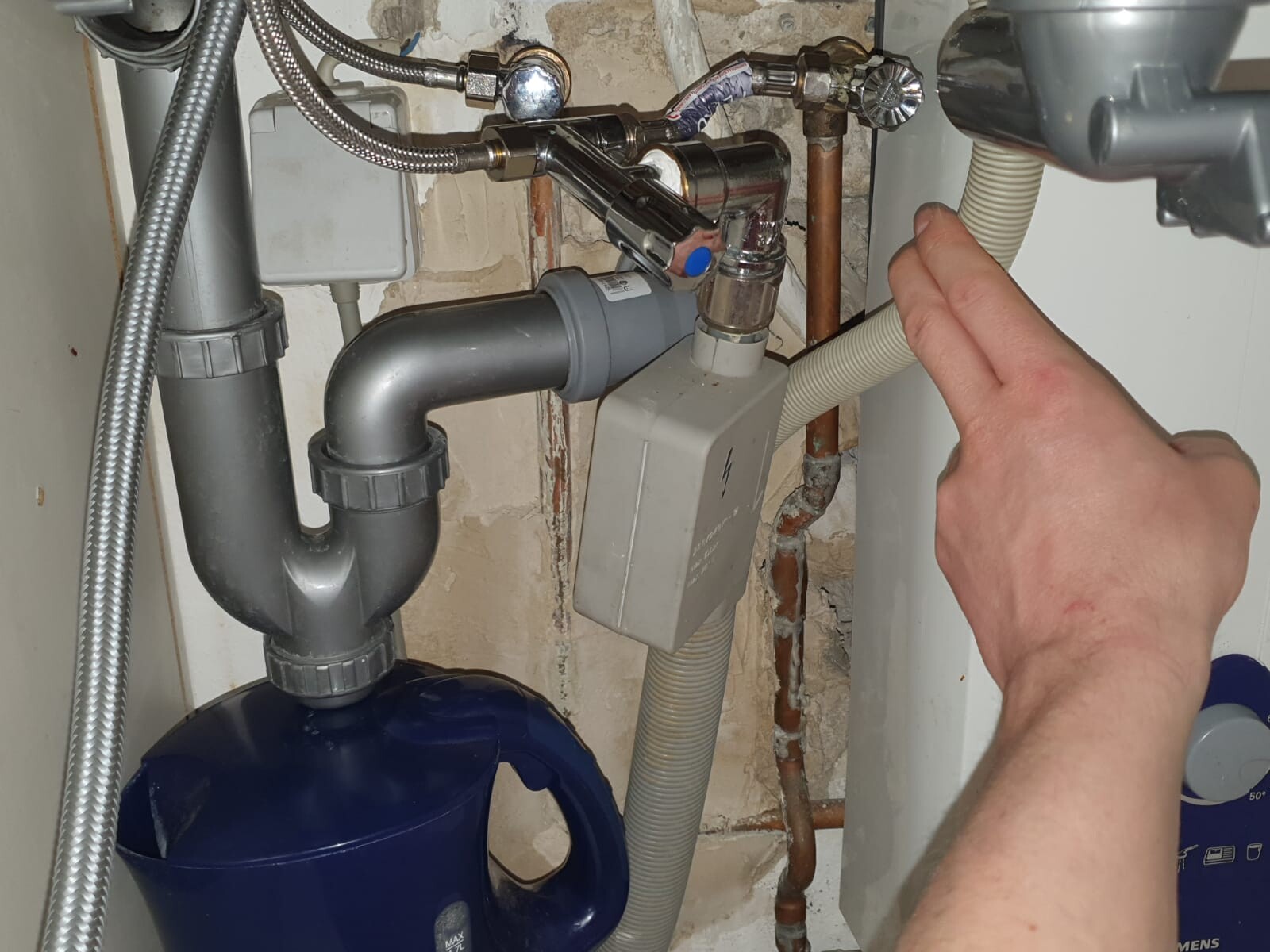 Under the kitchen sink: siphon, pipes, flexible hoses, hand pointing at shut-off valve.