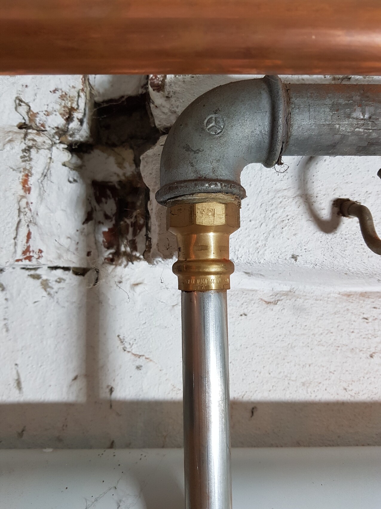 Water pipe: 90° metal elbow with brass compression coupling, vertical pipe below.