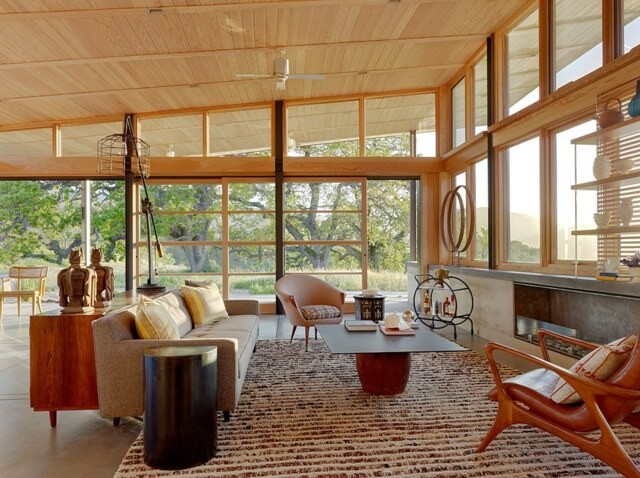 Bright living room with wooden ceiling, large windows, sofa, armchair, coffee table and rug.