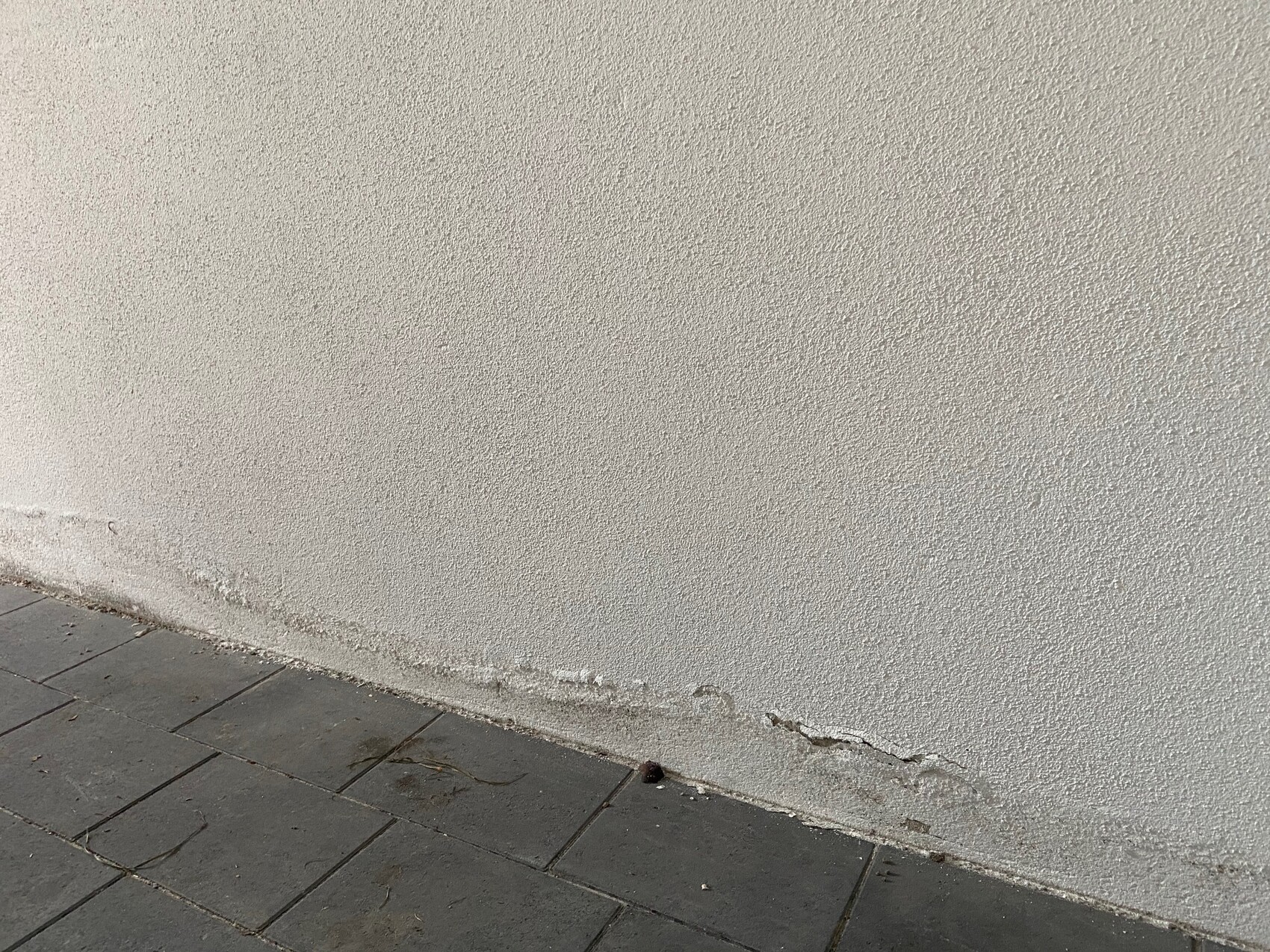 Beige rendered exterior wall with rough texture, cracks and spalling at the bottom.