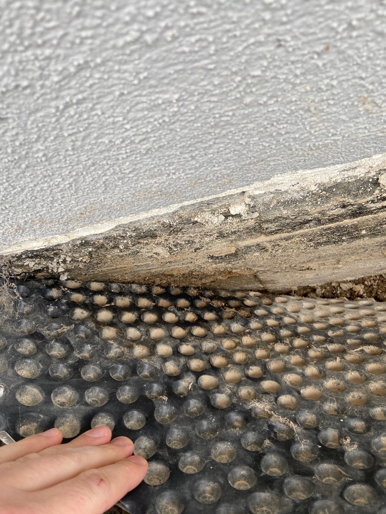 Bottom edge of a step with dust; below is an anti-slip studded mat, hand visible