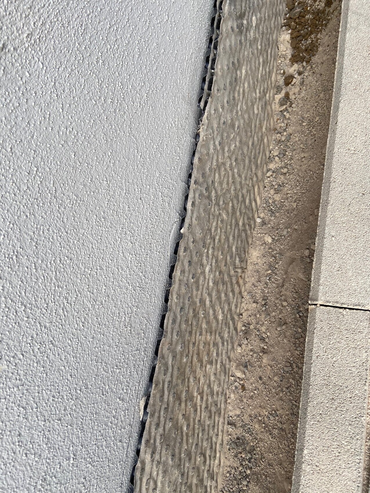 Narrow gap between wall on the left and ribbed metal profile on the right; soil next to it.