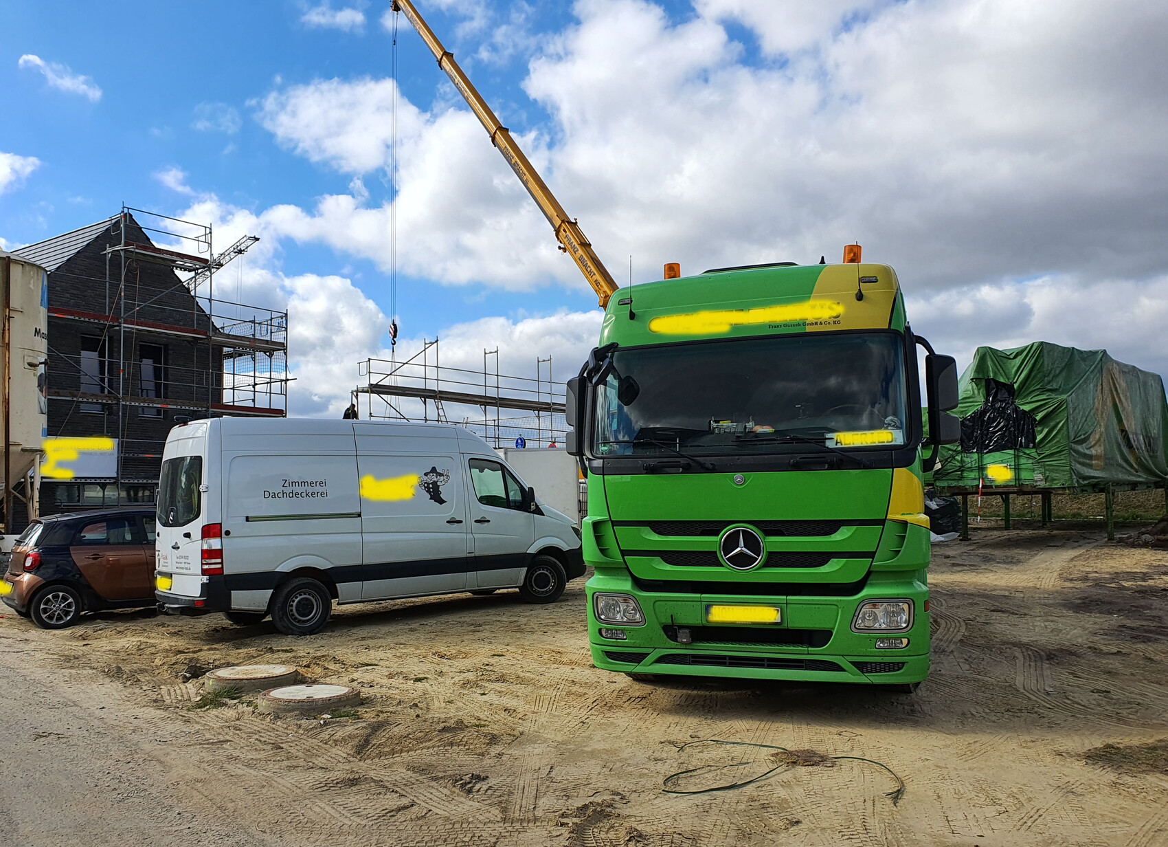 Construction site with green Mercedes truck, white van, scaffolding, and crane in front of unfinished house.
