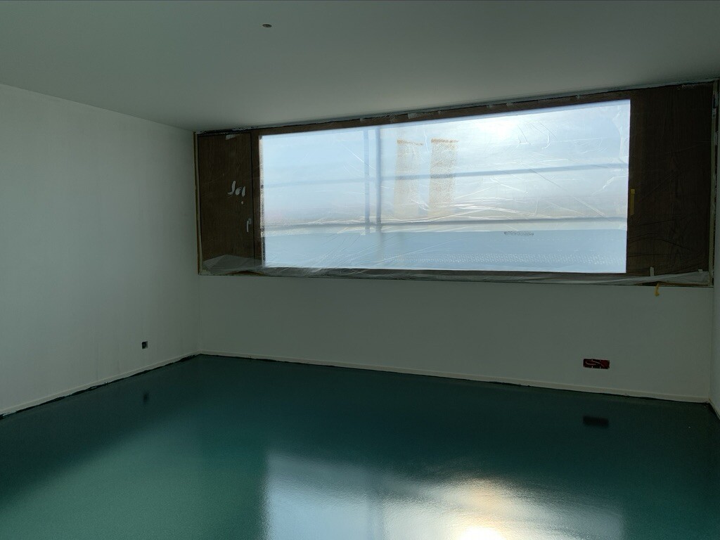 Empty renovation room with large window, green floor, and construction plastic on the window.