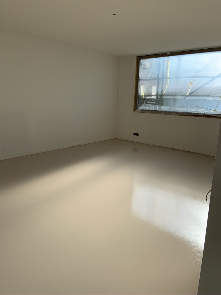 Empty white-painted room with large windows, shiny floor, outdoor construction site visible.