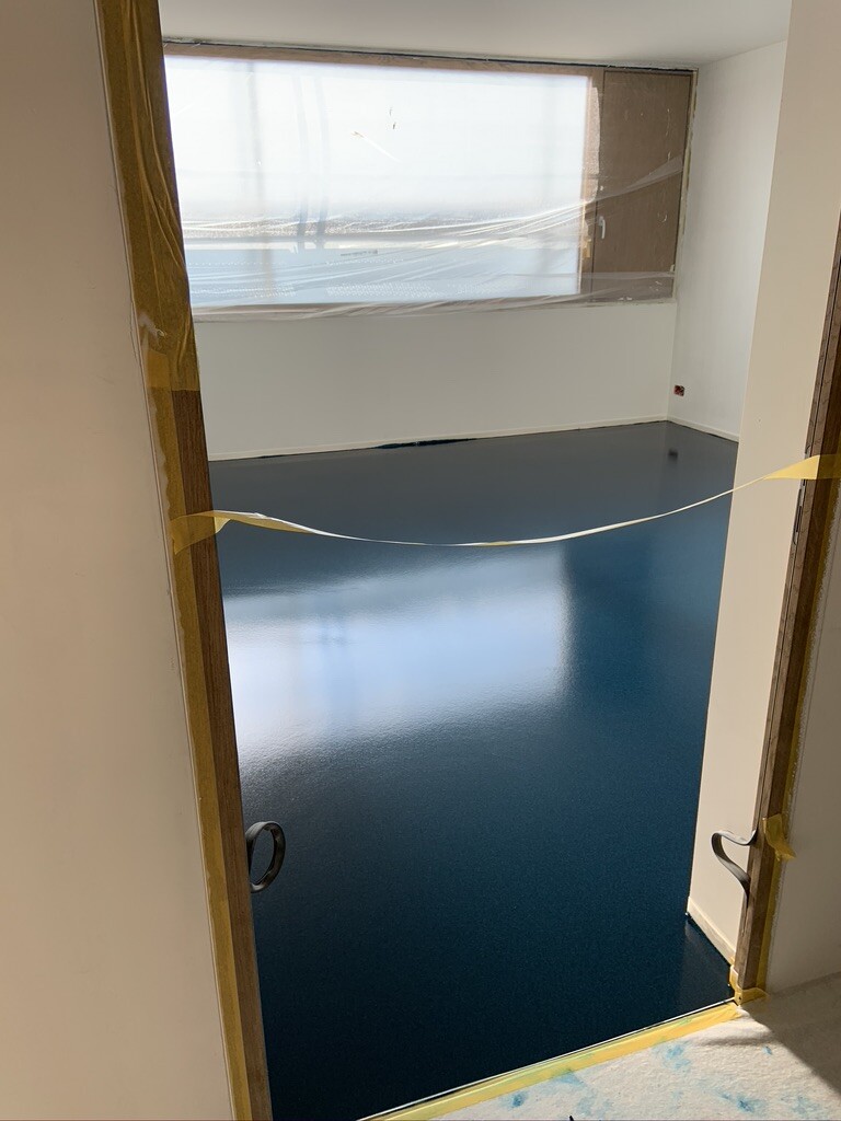 Empty renovation room with dark blue, glossy floor; window covered with plastic sheeting and caution tape.