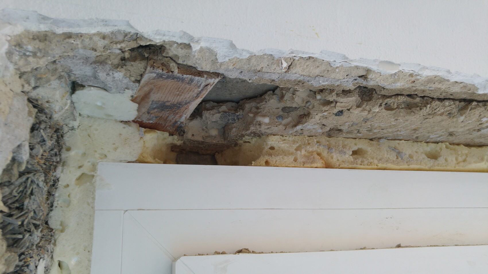 Open wall with flaking plaster, insulation and construction materials visible.