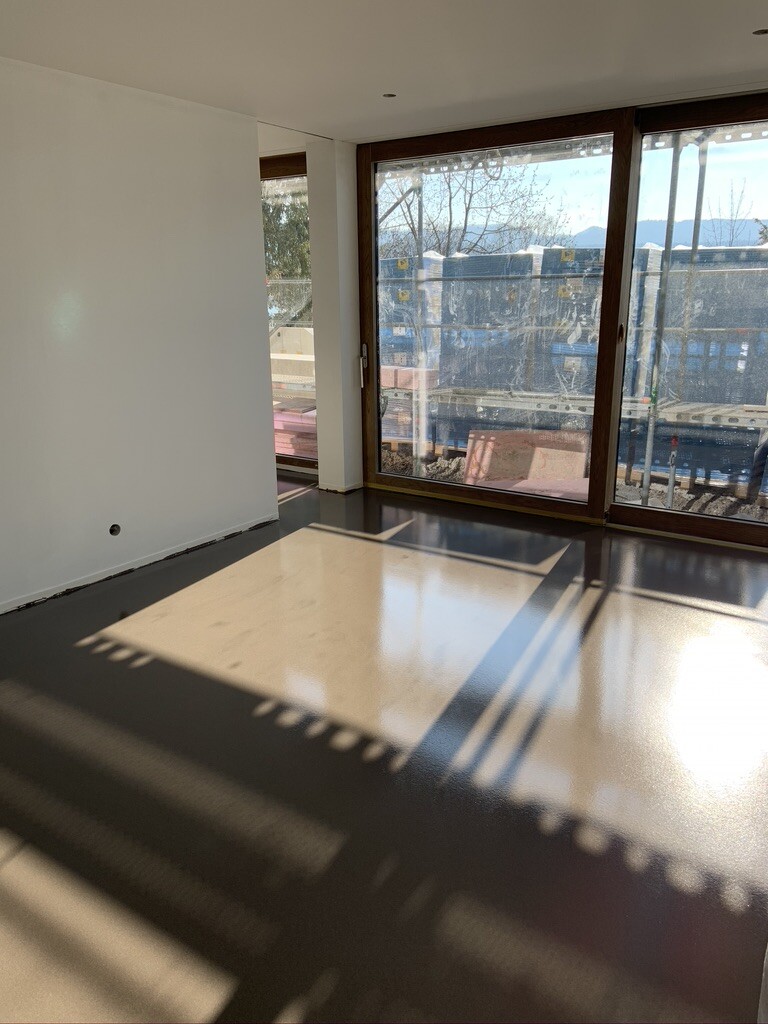 Bright empty interior with glass sliding doors; view outside to a construction site, sunlight.