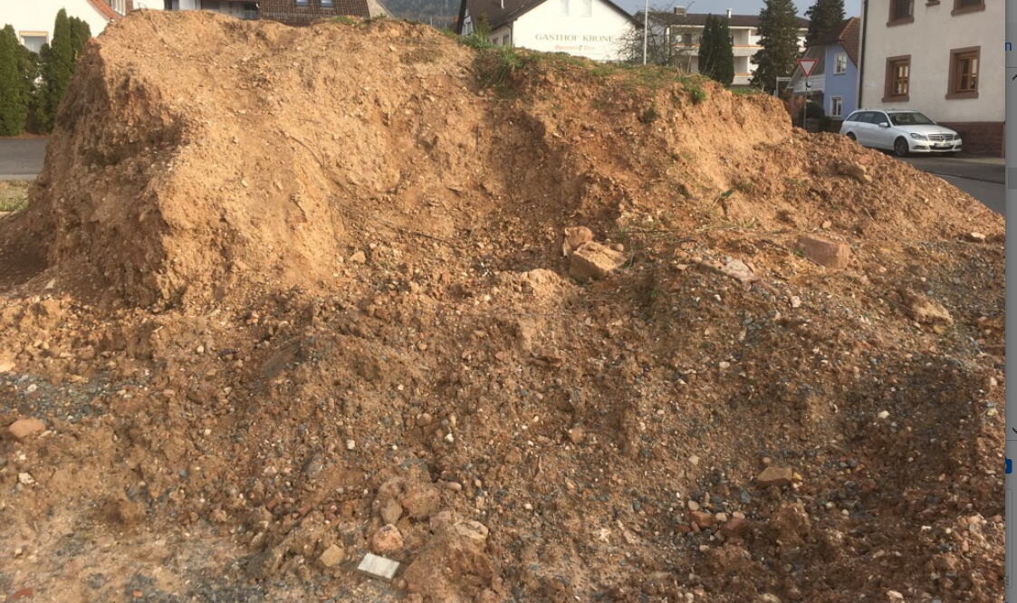 Großer Erdhügel auf Baustelle in Wohngegend, Bodenarbeiten vor Rohbau sichtbar.