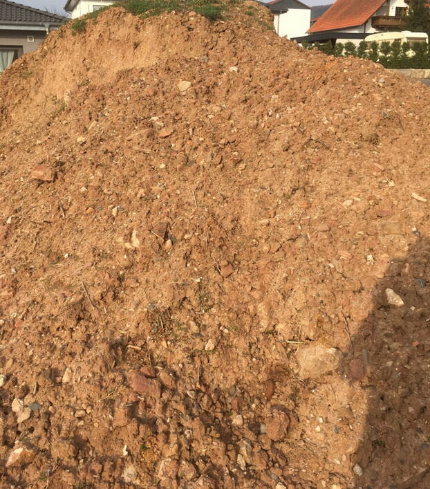 Großer Erdhügel auf Baugrundstück mit benachbarten Häusern im Hintergrund