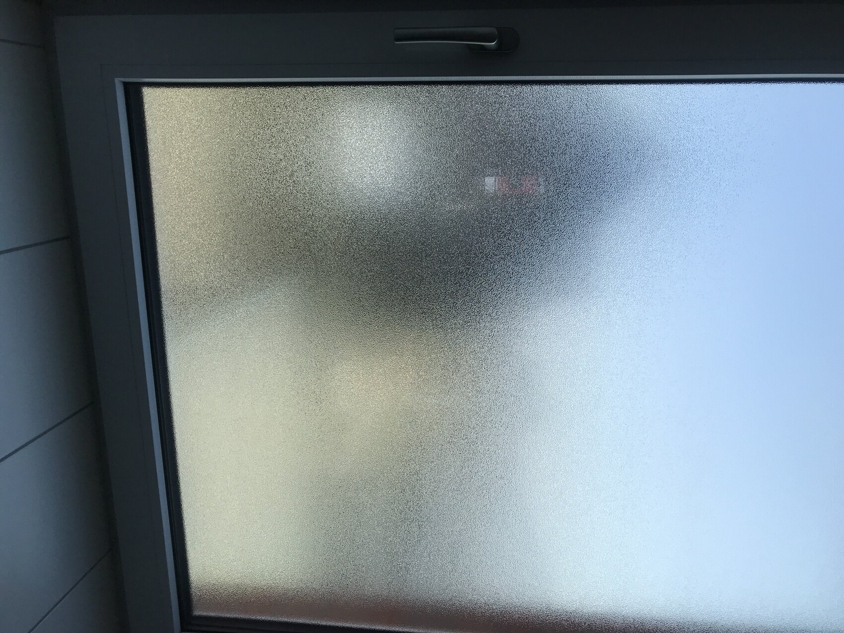 Milky window with frame; blurry silhouette behind glass, handle at the top.