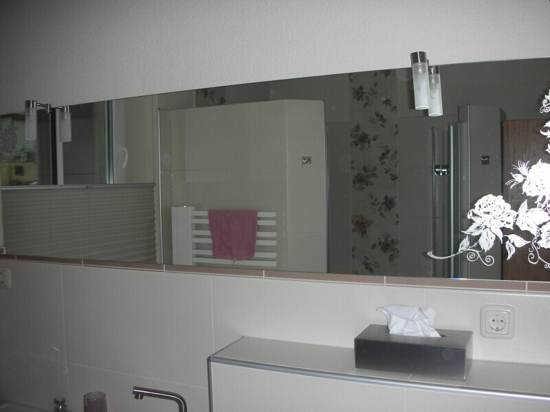 Bathroom with a large mirrored wall, pink towel on the radiator, washbasin with tissue box.