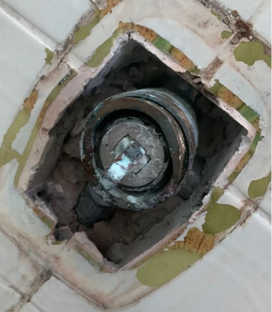 Offener Sanitäranschluss in einer beschädigten Badezimmerwandfliese.