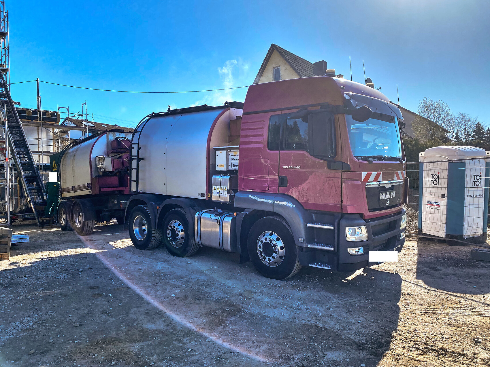 Large pink concrete mixer truck stands on a construction site next to scaffolding