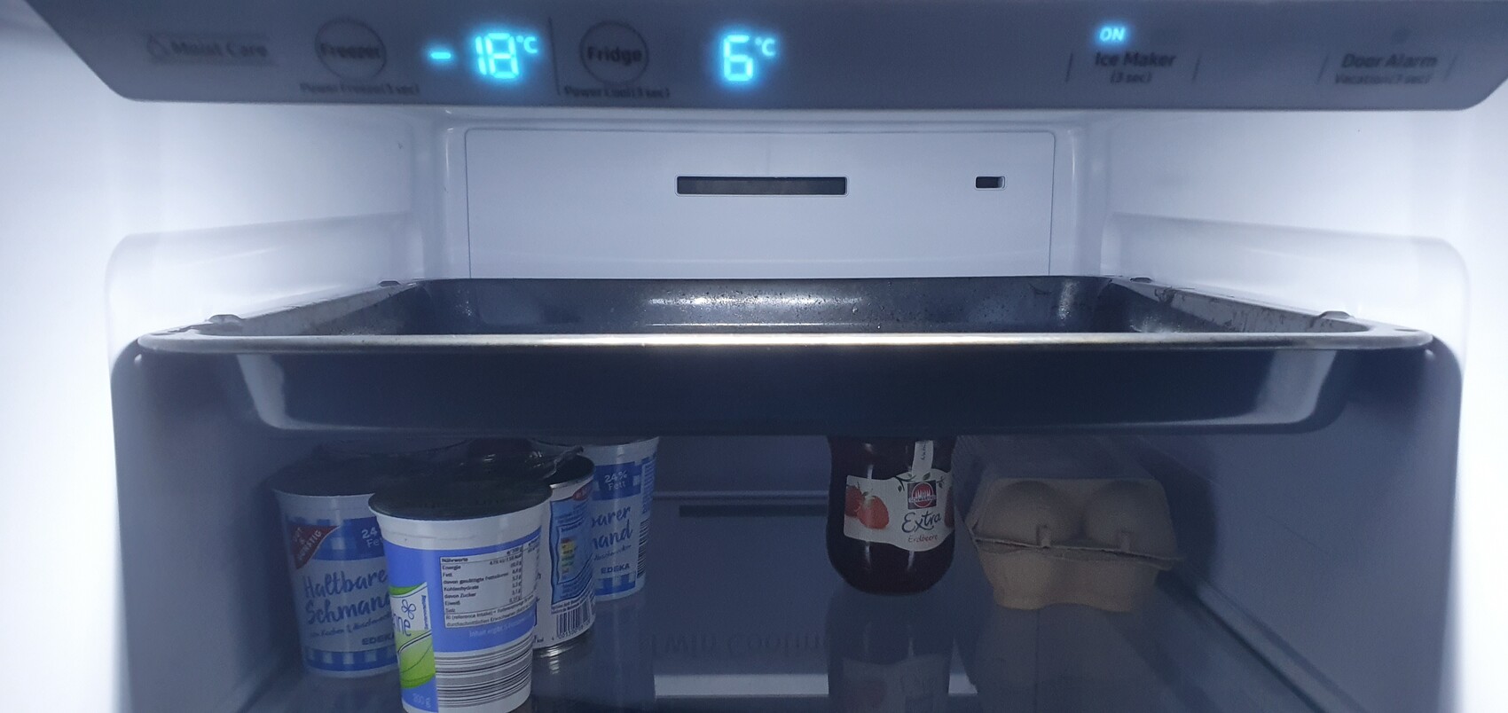 Open freezer compartment with yogurt cups, bottle and egg carton; display shows -18°C (0°F).