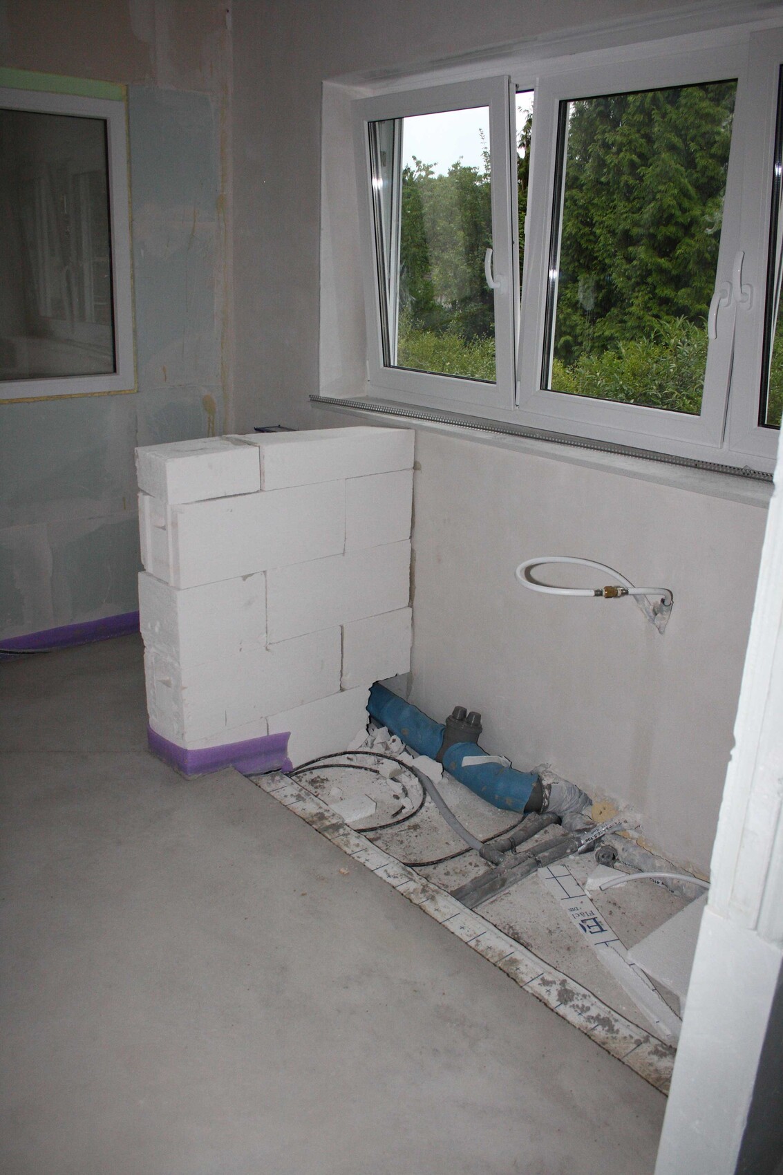 Internal partition wall made of polystyrene blocks next to window; pipes and cables visible on the floor.