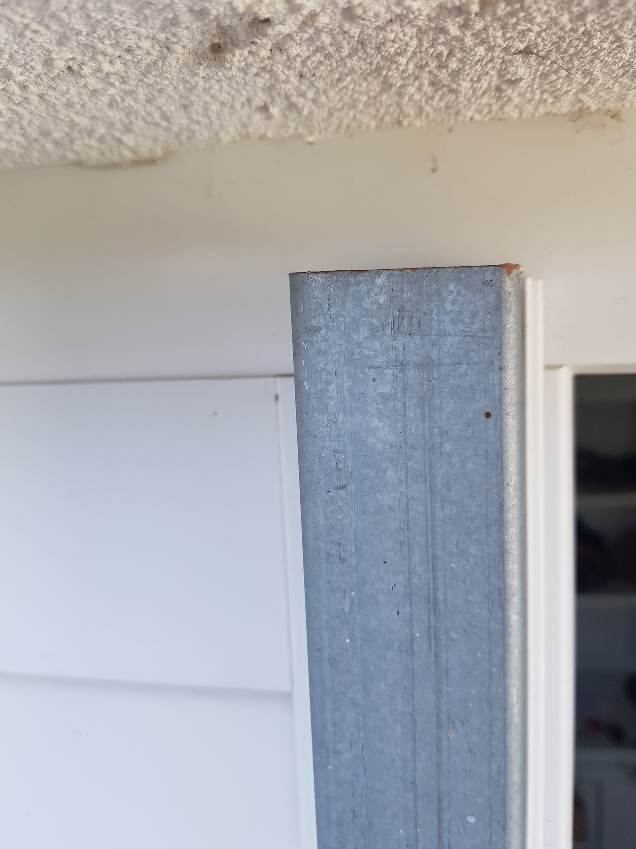 Vertical, gray galvanized metal post next to the door opening; rusty top edge visible.