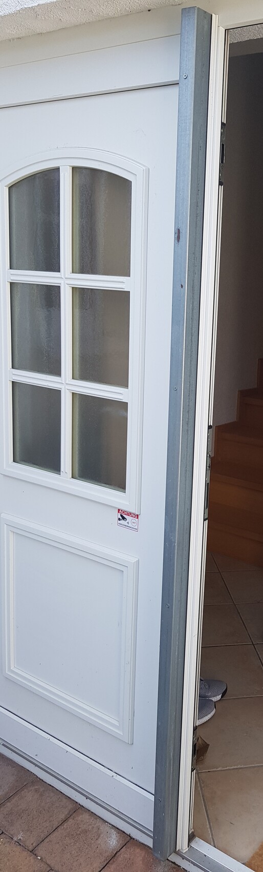 White door with six windows, slightly open; interior area with staircase visible.