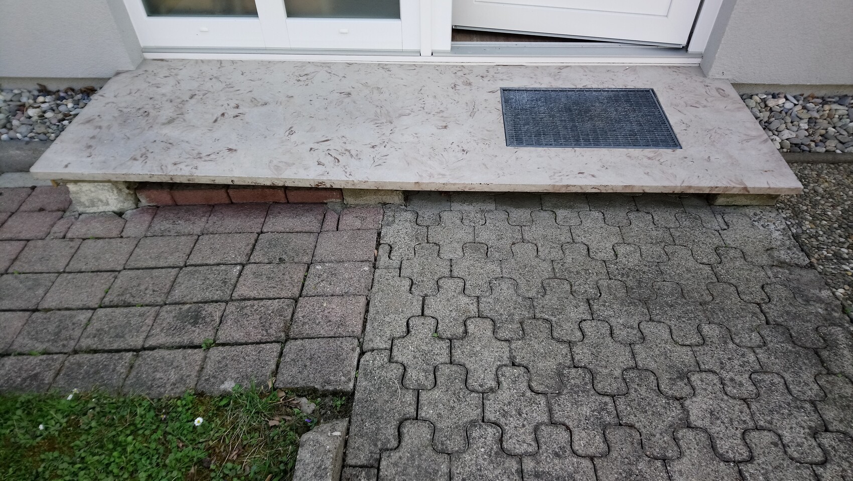 Light stone porch as a step in front of the front door with metal mesh; paved path in front.