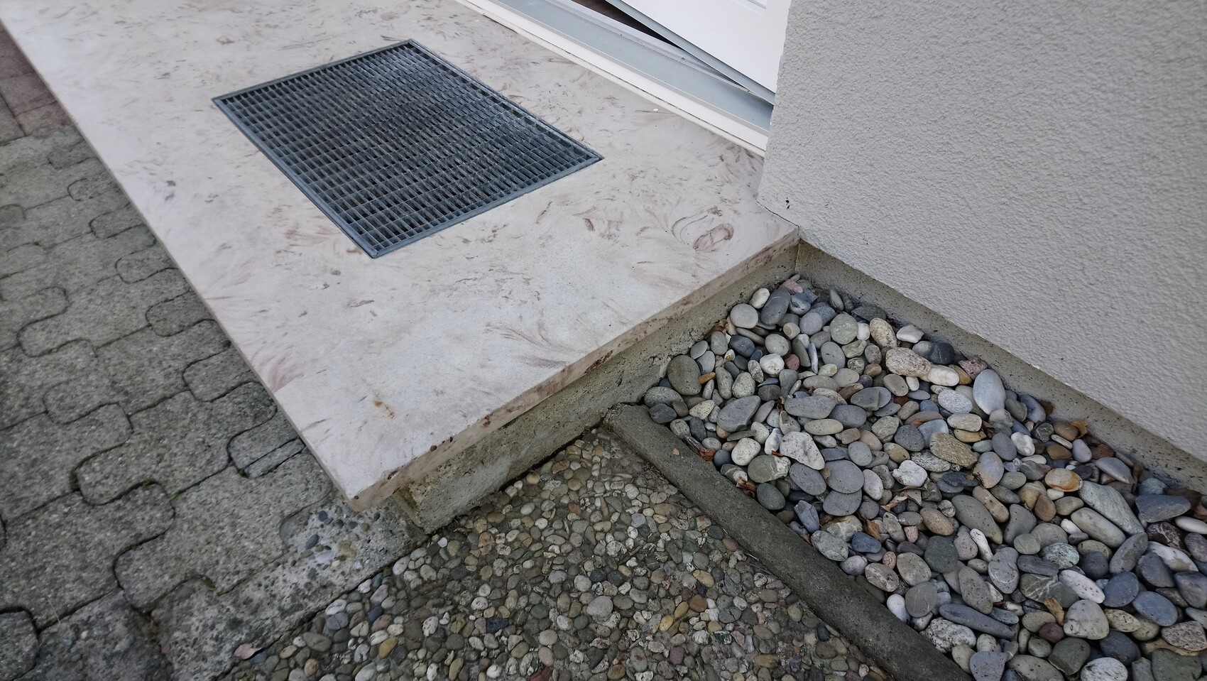 Entrance with beige marble floor tile, metal grate and gravel stone floor beside it.