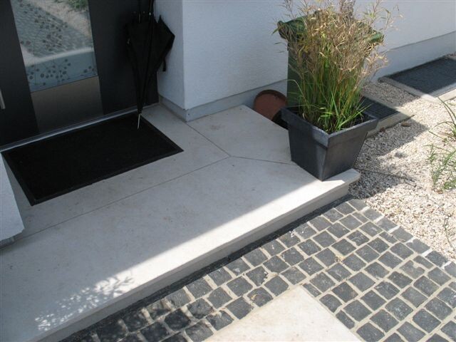 Entrance area with light steps, umbrella, planter with grass in front of the door.