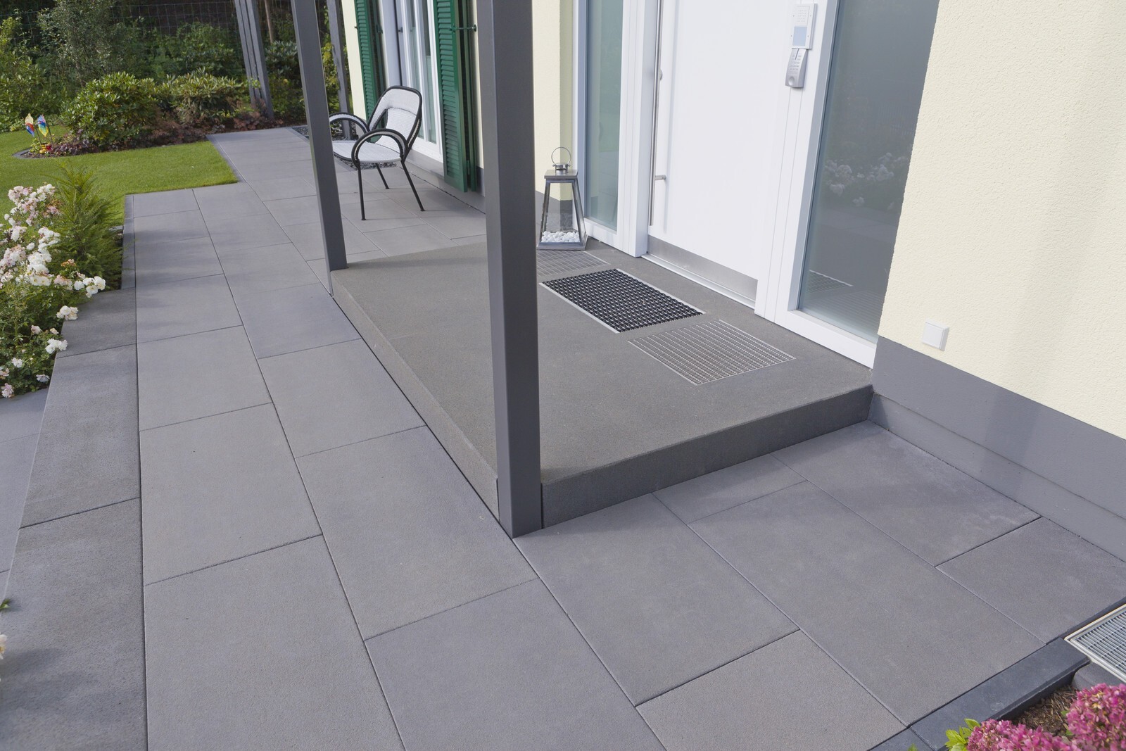 Modern terrace in front of a house: gray large-format paving slabs, chair, lantern, and glass door.