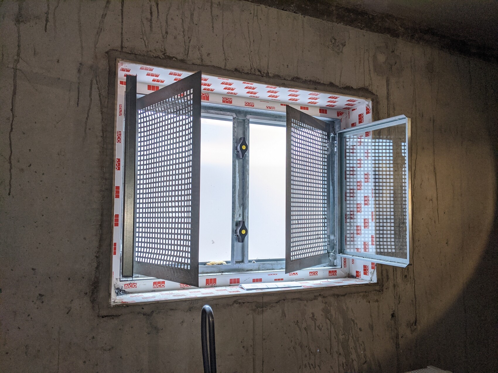 Open window with perforated metal grilles in an unfinished construction wall, construction phase visible.